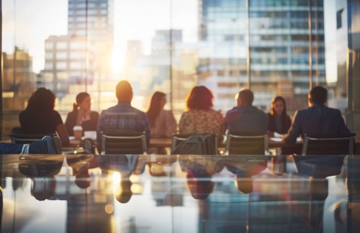 A group of employees sitting together at a meeting by a large window overlooking the city.