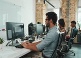 A row of employees sitting at desks using desktop computers
