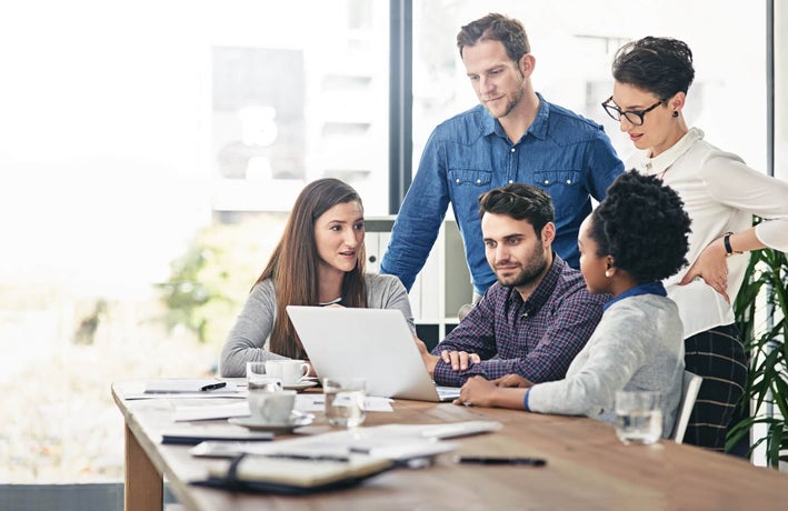 Group of employees standing around a single laptop