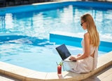 Woman sitting at a pool working on her laptop