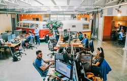 Employees working at computers in an open plan studio-style office with two minivans in the background.