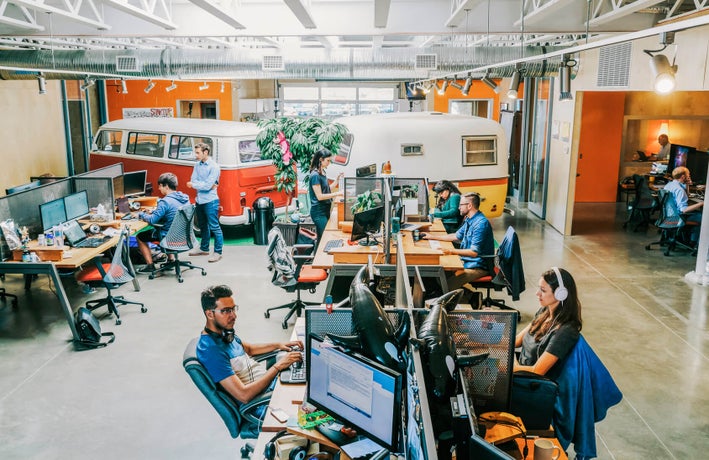 Employees working at computers in an open plan studio-style office with two minivans in the background.