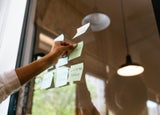 A single hand sticking written post it notes onto a window.