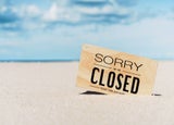 Sign reading 'Sorry we are closed' in the sand at the beach
