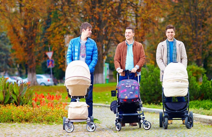 New dads pushing babies in prams through a park
