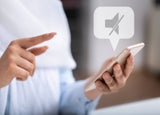 A shot of a pair of hands with one holding a white phone, with a no sound notification bubble above.