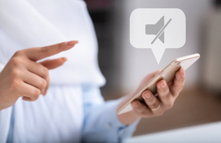 A shot of a pair of hands with one holding a white phone, with a no sound notification bubble above.