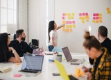 Team meeting with leader presenting by white board with post it notes.