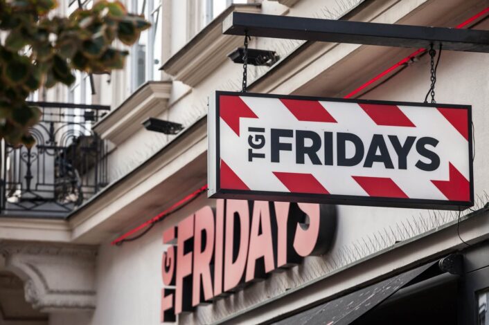 A shot of the outside of TGI Fridays restaurant with a hanging sign displayed prominently on the side.
