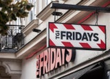 A shot of the outside of TGI Fridays restaurant with a hanging sign displayed prominently on the side.