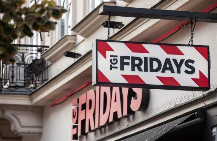 A shot of the outside of TGI Fridays restaurant with a hanging sign displayed prominently on the side.