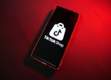 A smartphone device with a red backdrop displaying the TikTok Shop logo.