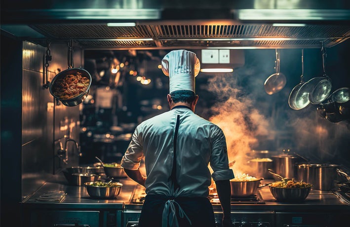 A man in a chef's uniform preparing food in a dark kitchen setting.