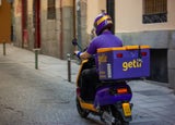 A Getir employee in company uniform driving a Getir-branded motorcycle on an empty street.