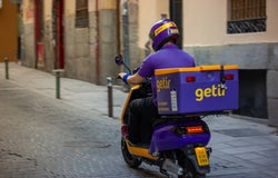 A Getir employee in company uniform driving a Getir-branded motorcycle on an empty street.