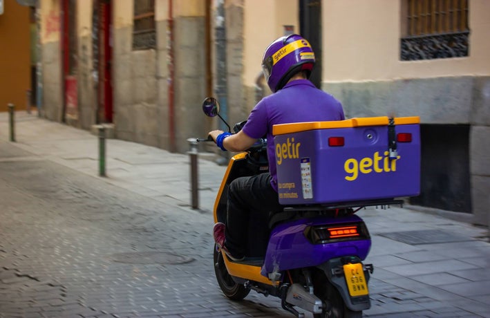 A Getir employee in company uniform driving a Getir-branded motorcycle on an empty street.