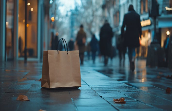 A lone brown paper bag sitting on the wet ground of a busy high street on a rainy day.