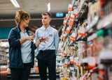 A store supervisor giving training to an employee in the middle of a supermarket aisle.