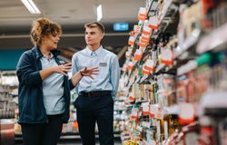 A store supervisor giving training to an employee in the middle of a supermarket aisle.