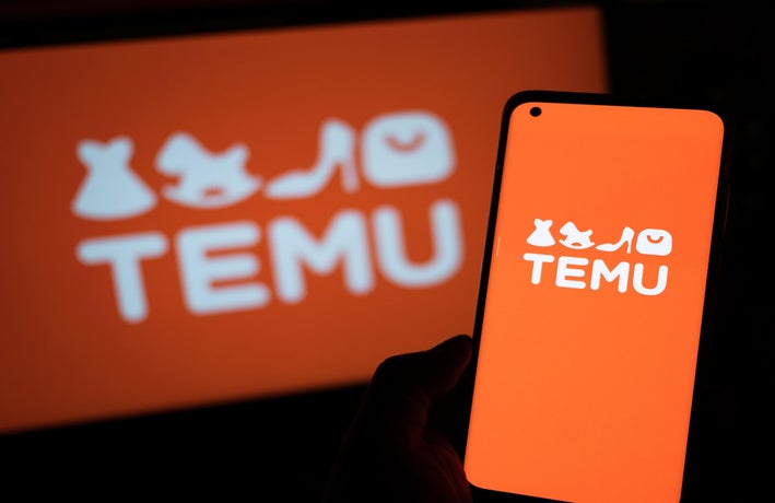 A smartphone device displaying the Temu logo against an orange background. The same also appears on a computer screen behind the phone.