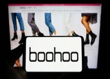 A smartphone device displaying the Boohoo logo against a backdrop of a computer screen with Boohoo product listings.