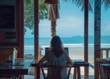 A woman sitting in a beachside cafe at her laptop