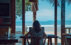 A woman sitting in a beachside cafe at her laptop