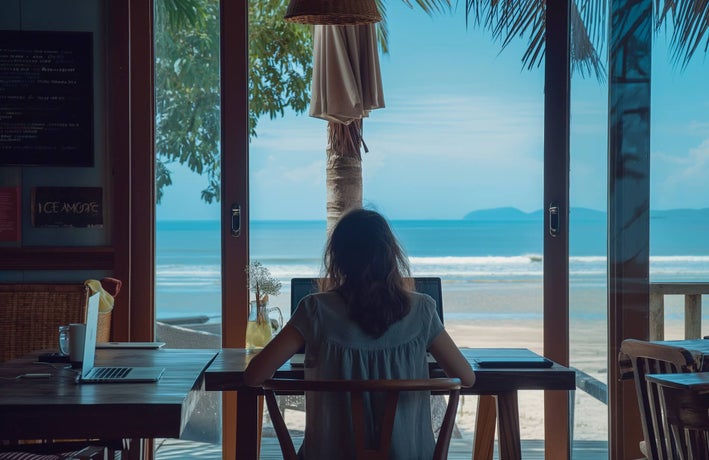 A woman sitting in a beachside cafe at her laptop