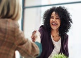 Two women in an office setting shaking hands.