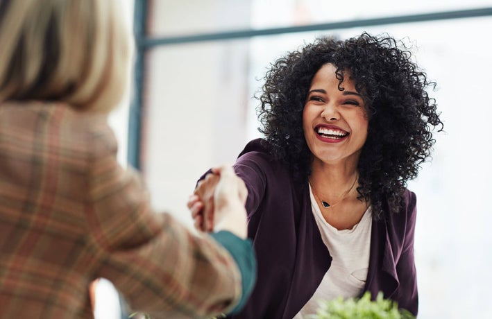 Two women in an office setting shaking hands.