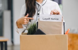 A woman with a white shirt standing behind a box of office supplies holding an envelope that reads 