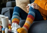 A shot of someone sitting on the sofa resting their feet on a coffee table filled with medicine and tissues.