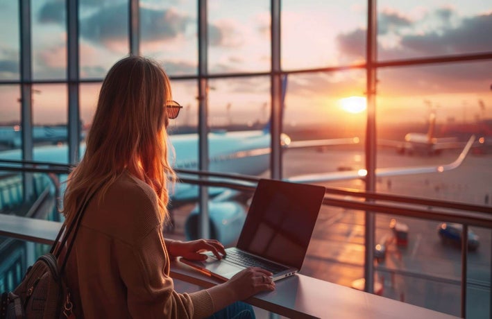 A woman sitting at the airport window facing the runway.