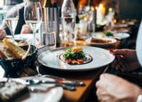 A gourmet meal on a white plate is set in front of a patron in a restaurant