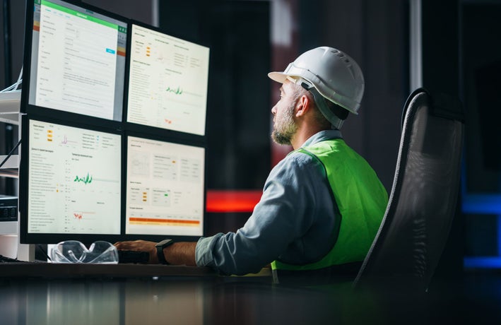 Construction worker looks at a computer screen showing various charts and graphs