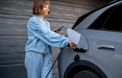 Woman charges her electric car near a house